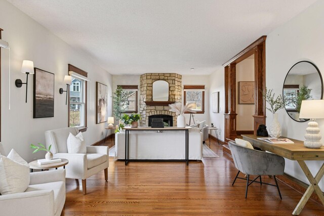 living room featuring a stone fireplace, baseboards, and wood finished floors