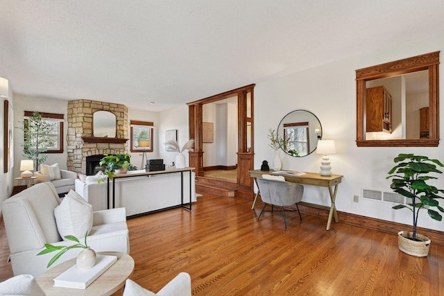 living room featuring a stone fireplace, baseboards, visible vents, and wood finished floors