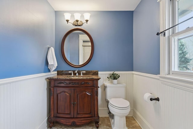 half bath with a wainscoted wall, toilet, and vanity