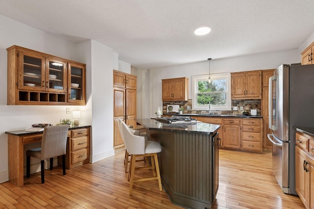 kitchen featuring a kitchen breakfast bar, light wood-type flooring, backsplash, a sink, and freestanding refrigerator