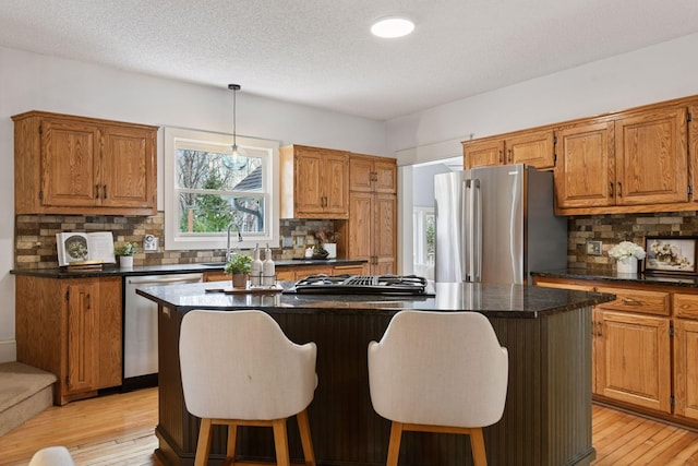 kitchen featuring a breakfast bar, appliances with stainless steel finishes, a center island, light wood-type flooring, and dark countertops