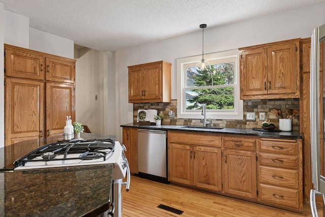kitchen with visible vents, dishwasher, brown cabinets, a sink, and gas range