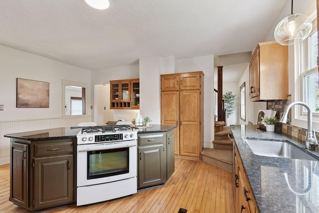 kitchen with white gas stove, dark stone counters, a kitchen island, a sink, and light wood-style floors