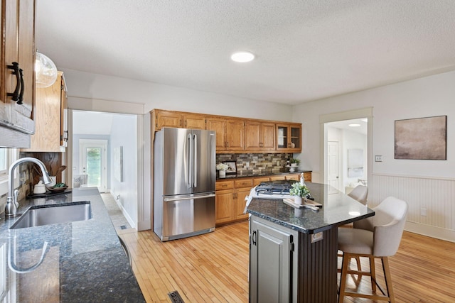 kitchen with a sink, freestanding refrigerator, a kitchen bar, wainscoting, and light wood-style flooring