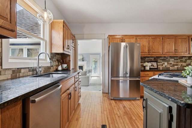 kitchen with brown cabinets, stainless steel appliances, tasteful backsplash, a sink, and light wood-style floors