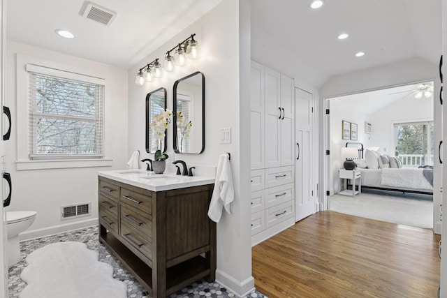 ensuite bathroom with ceiling fan, visible vents, vaulted ceiling, and wood finished floors