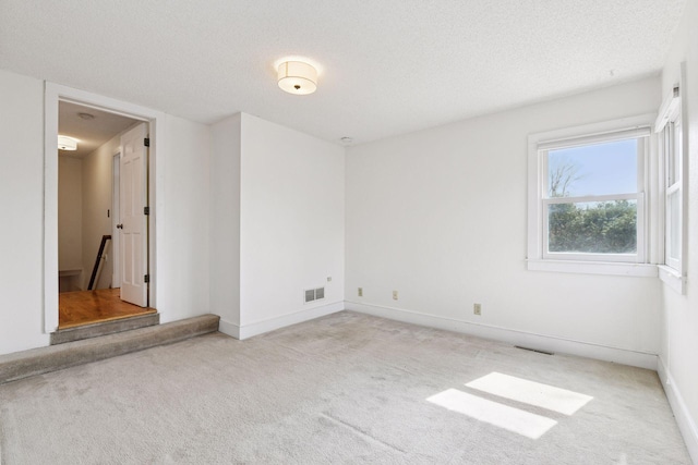 spare room with baseboards, visible vents, carpet, and a textured ceiling