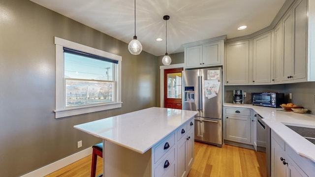 kitchen with pendant lighting, light wood-type flooring, stainless steel appliances, and a kitchen island