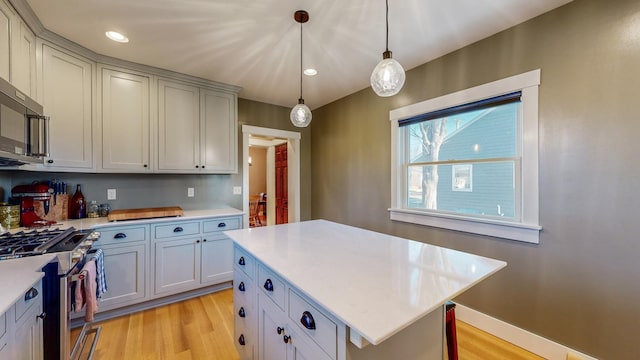 kitchen with gray cabinetry, hanging light fixtures, light hardwood / wood-style floors, a kitchen island, and stainless steel appliances