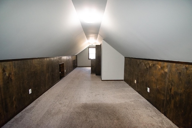 additional living space with wooden walls, light colored carpet, and lofted ceiling