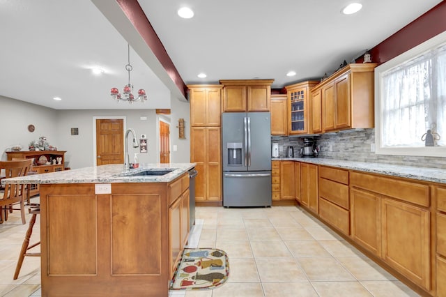 kitchen featuring light stone countertops, appliances with stainless steel finishes, a kitchen breakfast bar, a kitchen island with sink, and sink