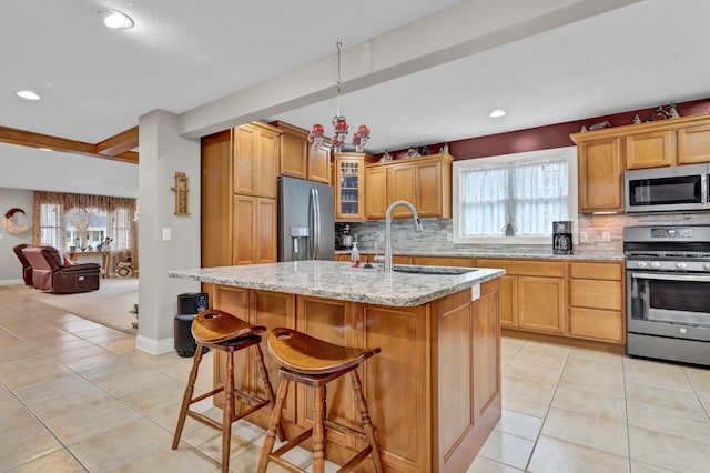 kitchen with sink, light stone counters, an island with sink, a breakfast bar, and appliances with stainless steel finishes