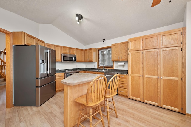 kitchen with a center island, stainless steel appliances, vaulted ceiling, and light hardwood / wood-style floors