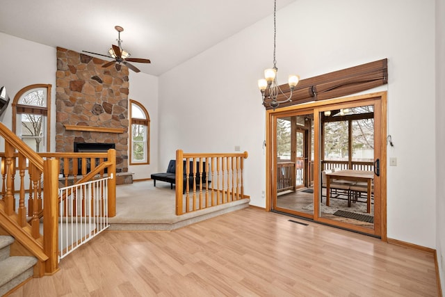 interior space featuring hardwood / wood-style floors, ceiling fan with notable chandelier, a stone fireplace, and lofted ceiling