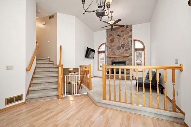 stairs featuring hardwood / wood-style flooring, ceiling fan with notable chandelier, and a stone fireplace