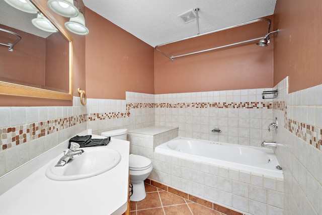 bathroom featuring tile patterned floors, a textured ceiling, tile walls, tiled bath, and toilet