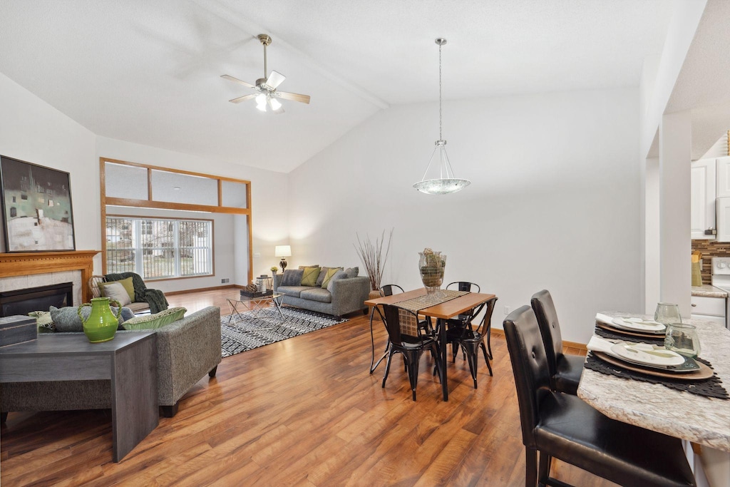 dining space featuring hardwood / wood-style floors, ceiling fan, lofted ceiling, and a tiled fireplace