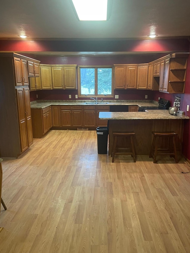 kitchen with kitchen peninsula, light wood-type flooring, a breakfast bar, sink, and black electric range