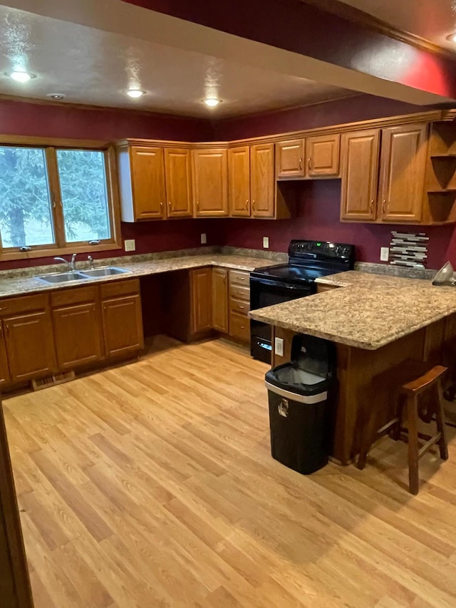 kitchen featuring a breakfast bar, light hardwood / wood-style flooring, sink, and black electric range