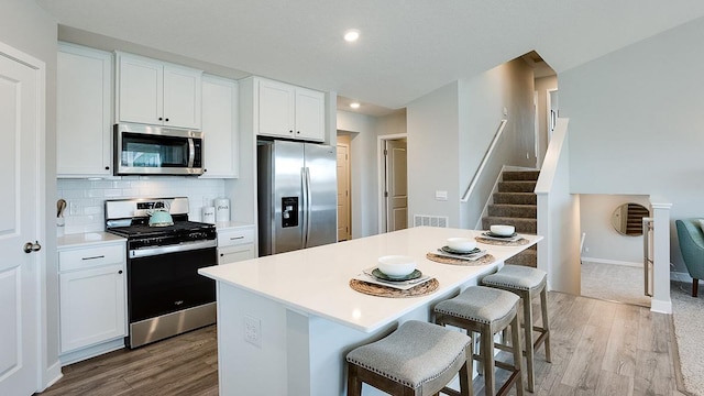 kitchen with a breakfast bar area, light wood-type flooring, tasteful backsplash, white cabinetry, and stainless steel appliances