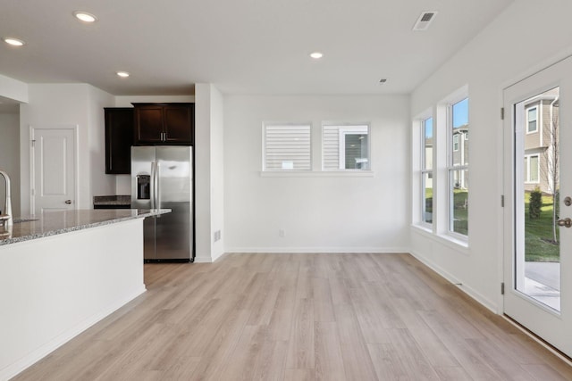 kitchen featuring light stone countertops, stainless steel refrigerator with ice dispenser, dark brown cabinetry, sink, and light hardwood / wood-style flooring