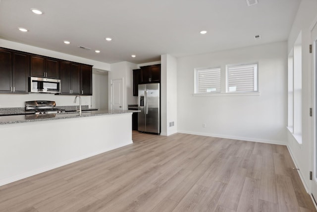 kitchen featuring appliances with stainless steel finishes, light wood-type flooring, light stone counters, dark brown cabinetry, and sink