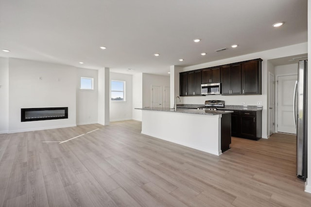 kitchen featuring a center island with sink, dark brown cabinetry, appliances with stainless steel finishes, and light hardwood / wood-style flooring