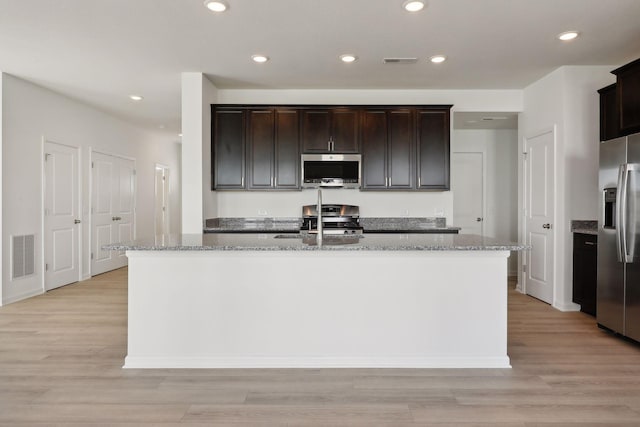 kitchen featuring light stone countertops, a center island with sink, stainless steel appliances, and light hardwood / wood-style floors