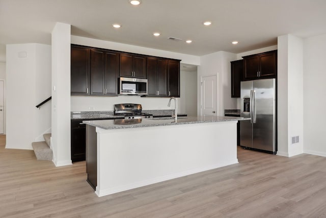 kitchen with appliances with stainless steel finishes, light wood-type flooring, a center island with sink, and dark brown cabinetry