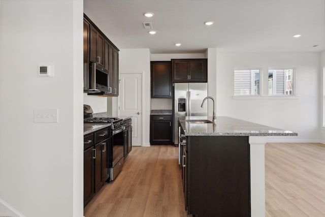 kitchen featuring gas stove, sink, light hardwood / wood-style floors, and an island with sink