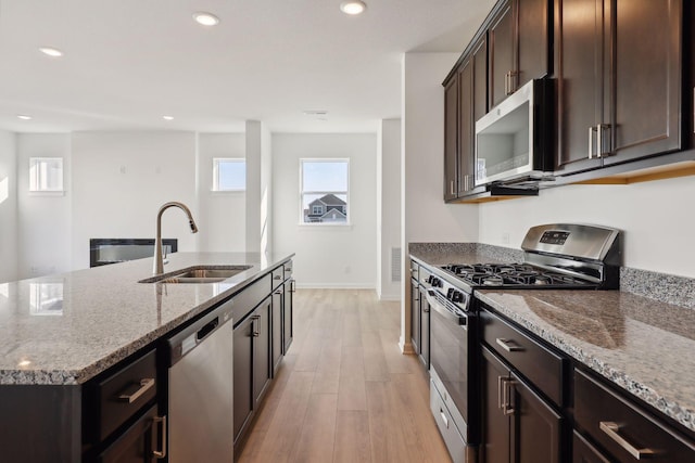 kitchen with sink, stainless steel appliances, light stone counters, light hardwood / wood-style flooring, and a kitchen island with sink