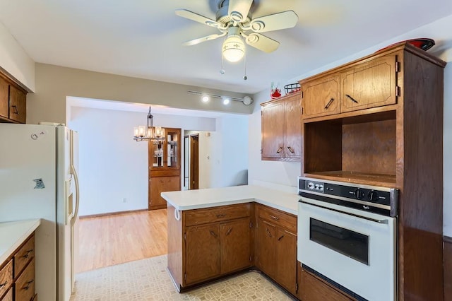 kitchen with ceiling fan with notable chandelier, pendant lighting, white appliances, kitchen peninsula, and light wood-type flooring