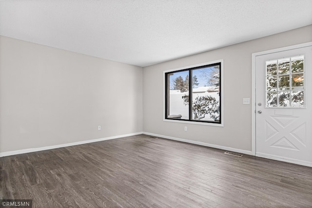 empty room with dark hardwood / wood-style flooring, a textured ceiling, and a wealth of natural light