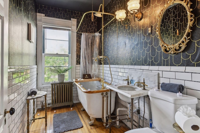 bathroom featuring radiator heating unit, hardwood / wood-style flooring, a wealth of natural light, and tile walls