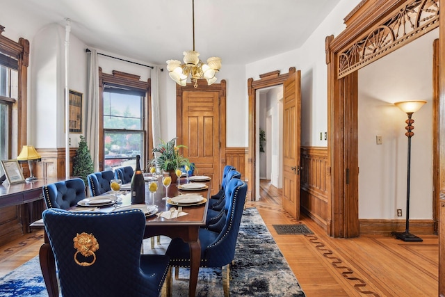 dining room featuring a notable chandelier, light hardwood / wood-style floors, and wooden walls