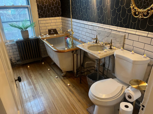 full bath with tile walls, a bath, toilet, radiator heating unit, and hardwood / wood-style flooring