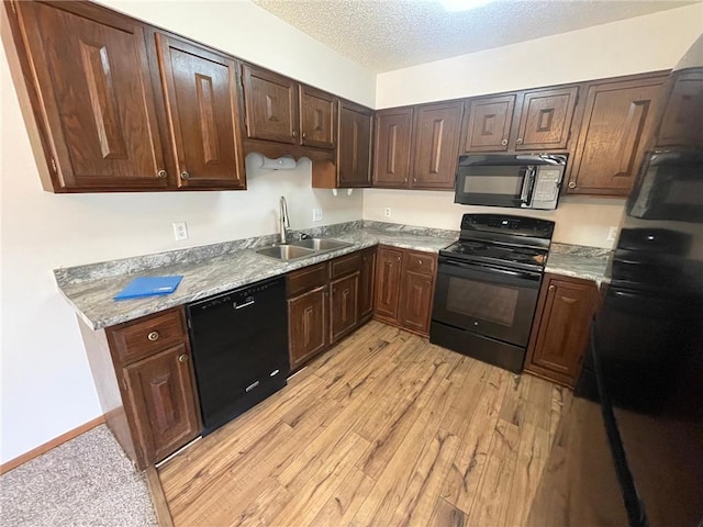 kitchen with black appliances, sink, light stone countertops, a textured ceiling, and light hardwood / wood-style floors