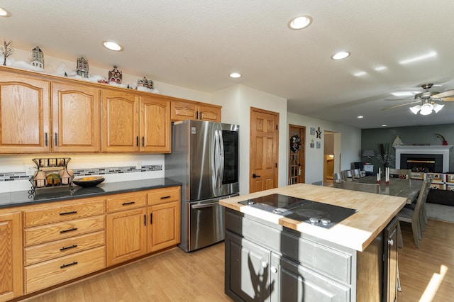 kitchen with stainless steel refrigerator, tasteful backsplash, light wood-type flooring, ceiling fan, and black electric cooktop