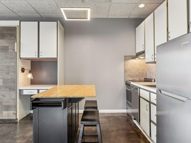 kitchen featuring a drop ceiling, a kitchen island, range hood, stainless steel fridge, and white cabinets