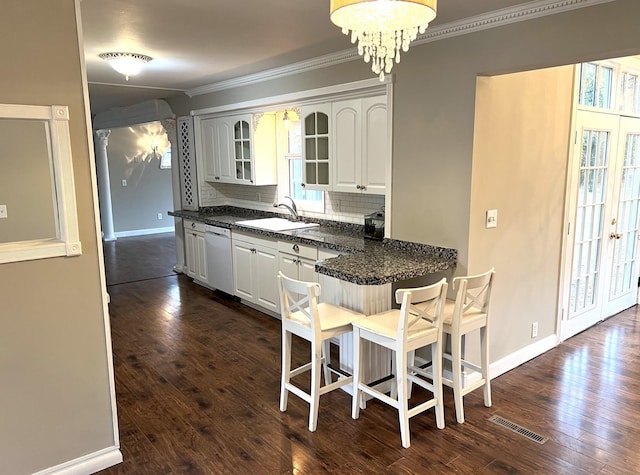 kitchen with white dishwasher, sink, tasteful backsplash, a kitchen bar, and white cabinetry