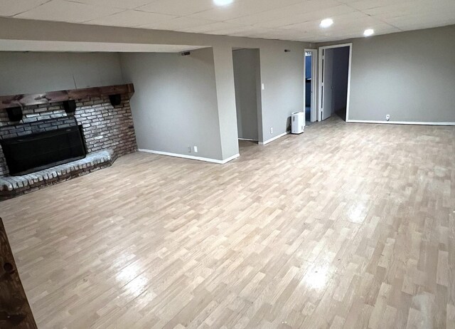 unfurnished living room featuring a drop ceiling, light wood-type flooring, and a brick fireplace