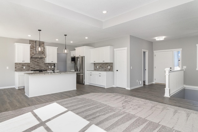 kitchen with wall chimney range hood, stainless steel appliances, dark hardwood / wood-style floors, and an island with sink