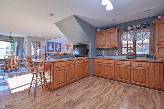 429 Bridge Ave, Warren, MN 56762 - kitchen featuring a peninsula, brown cabinetry, light wood-type flooring, a kitchen bar, and light countertops