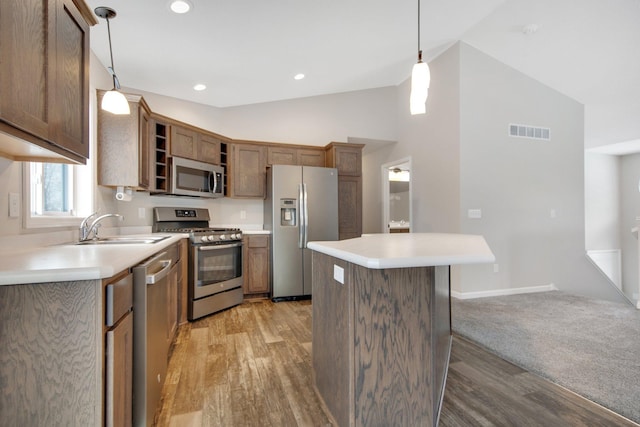 kitchen featuring appliances with stainless steel finishes, light wood-type flooring, sink, a kitchen island, and hanging light fixtures