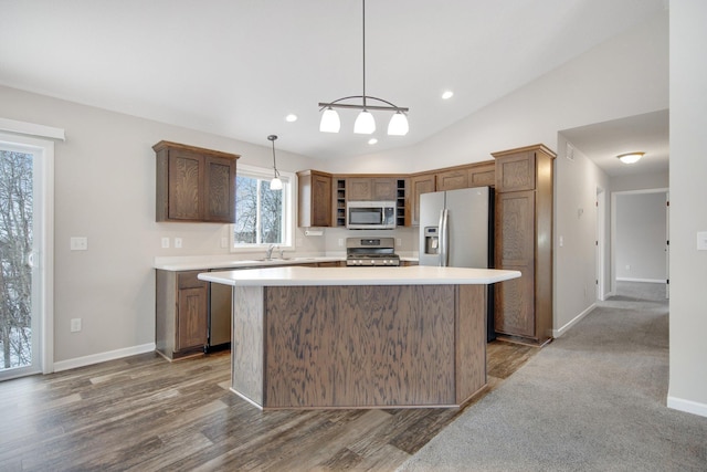 kitchen featuring a kitchen island, stainless steel appliances, hanging light fixtures, and vaulted ceiling