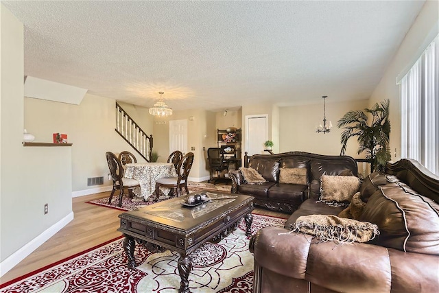 living room featuring a healthy amount of sunlight, light hardwood / wood-style floors, a textured ceiling, and an inviting chandelier