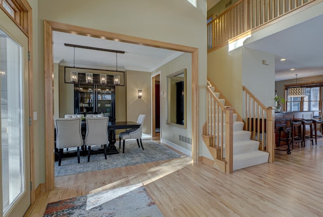 dining area featuring crown molding, a towering ceiling, a chandelier, and light hardwood / wood-style floors