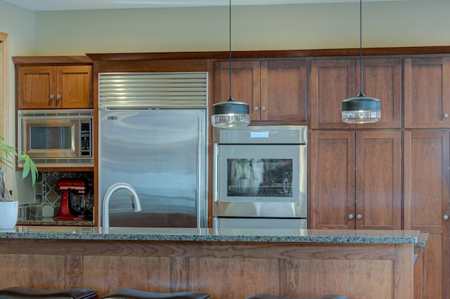 kitchen featuring built in appliances, pendant lighting, and stone countertops