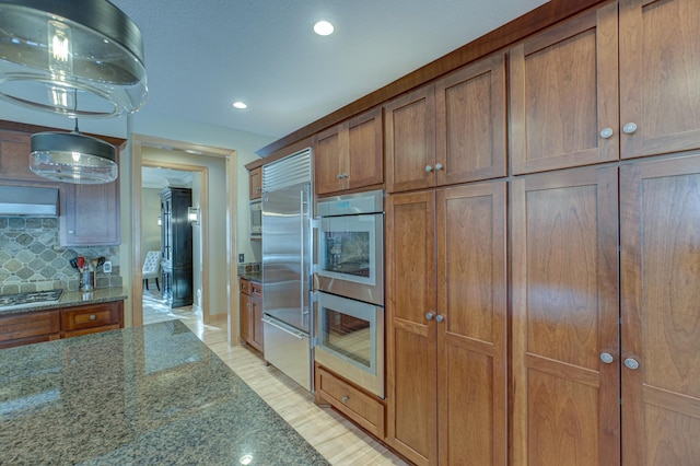 kitchen featuring appliances with stainless steel finishes, pendant lighting, dark stone countertops, and decorative backsplash