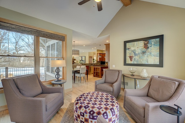 living room with beamed ceiling, ceiling fan, plenty of natural light, and light wood-type flooring